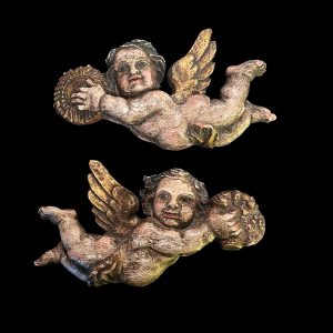 Pair of vintage wooden cherub wall plaques with painted and gilt finish, each shown in a flying pose holding a sunburst or flowers.