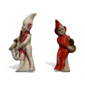 Two 1950s Japanese bisque pixie musician figurines, one playing a saxophone and one holding cymbals, with hand-painted red and gold details.